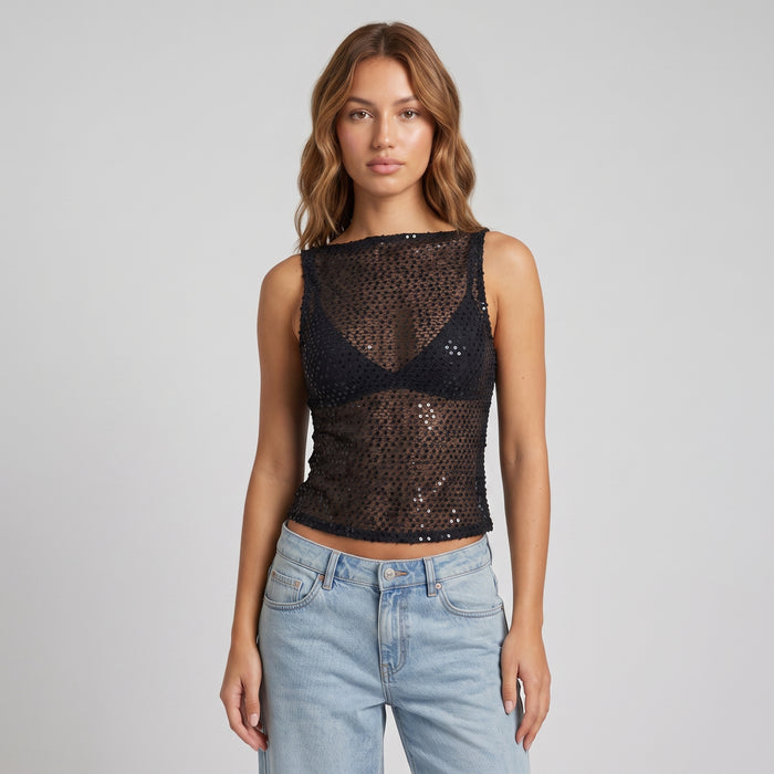 A woman modeling a black sequined mesh sleeveless crop top with a boat neckline, paired with light-wash blue jeans, against a solid light gray background.